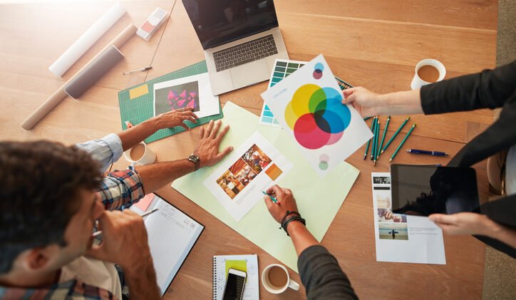 Top view shot of young designers discussing the color palette. Creative team brainstorming around table working together on new project.